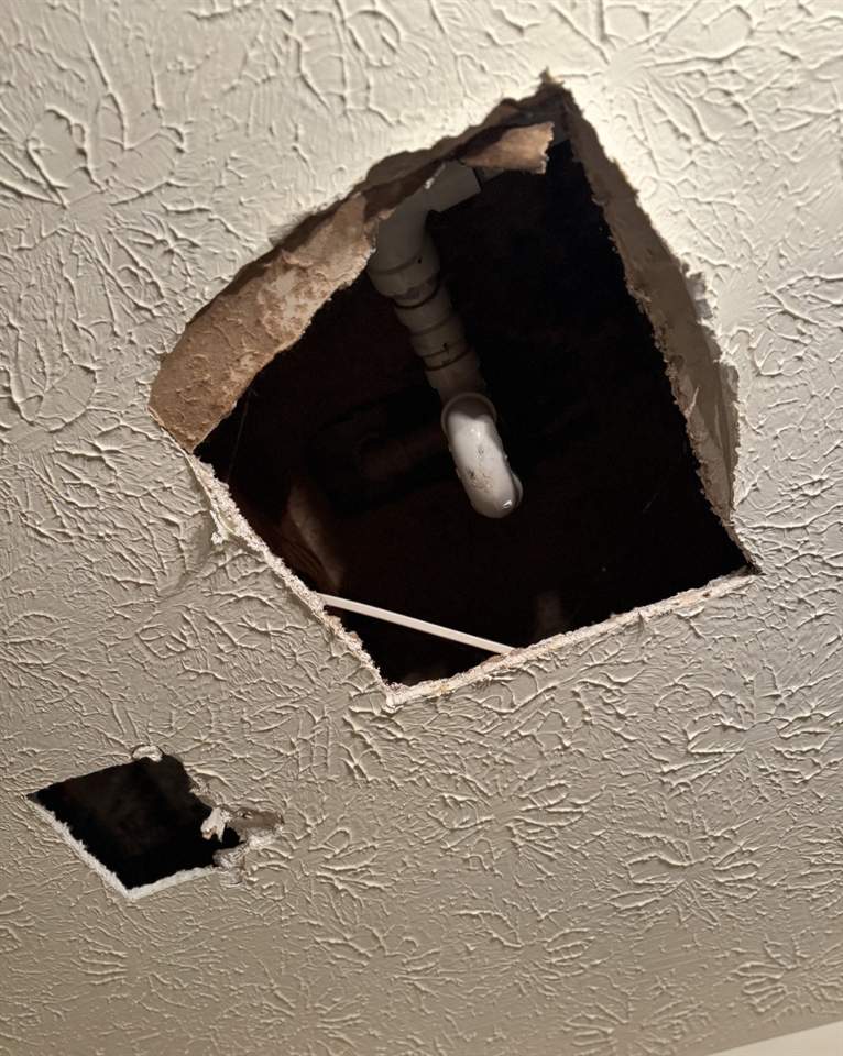 Ceiling opened up with drywall cut away exposing a leaking pipe