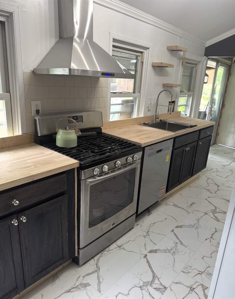 Remodeled kitchen with butcher block counters, dark cabinets and marble-look tile floor